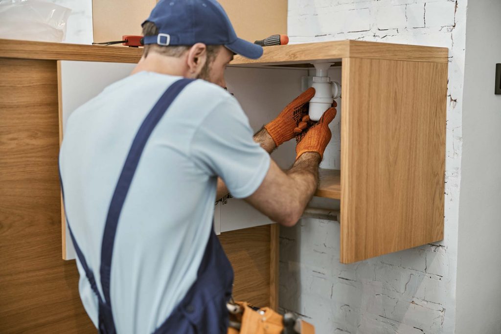 male-plumber-in-cap-repairing-pipe-in-kitchen-MFL8ZXU.jpg